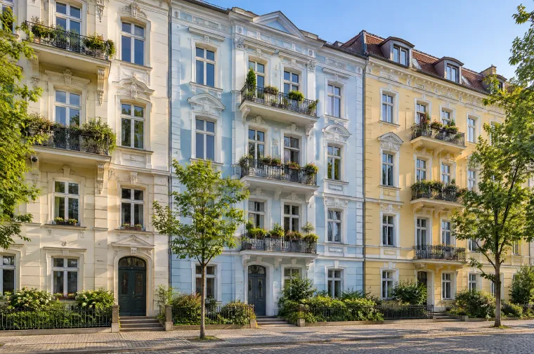 Straße mit sanierten Altbau-Mehrfamilienhäusern in Pastellfarben, mit Stuckfassaden, Balkonen und Straßenbäumen